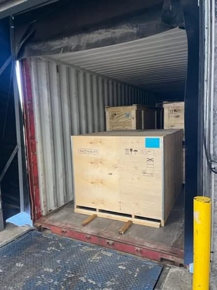 A crated Novair oxygen plant on a wooden pallet at the mouth of a shipping container, waiting to be pushed in.