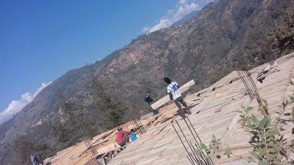 Two workers carry timber shuttering across the deck of the new floor, high above a forested valley.