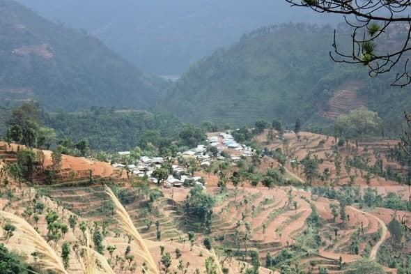 A valley of terraced fields with a cluster of tents and shelters gathered on flat ground at its centre.