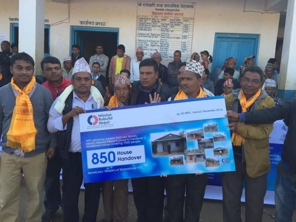 Men hold a large printed board reading 850 House Handover, illustrated with photographs of completed houses.