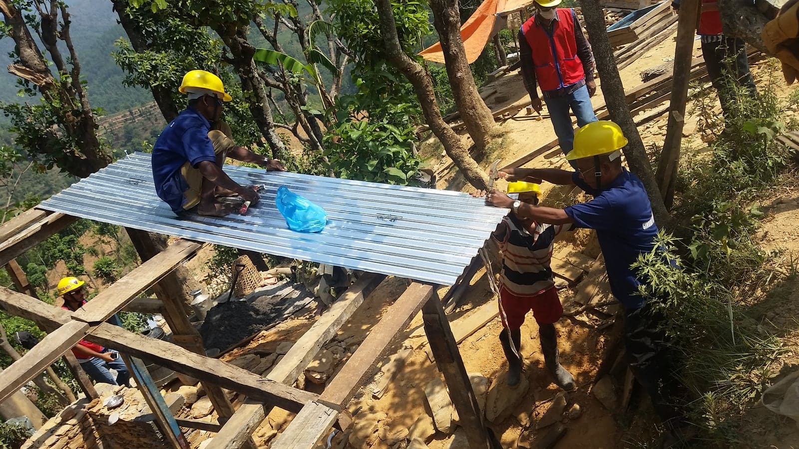 Four men lift and nail a corrugated steel sheet onto a timber roof frame on a steep slope.