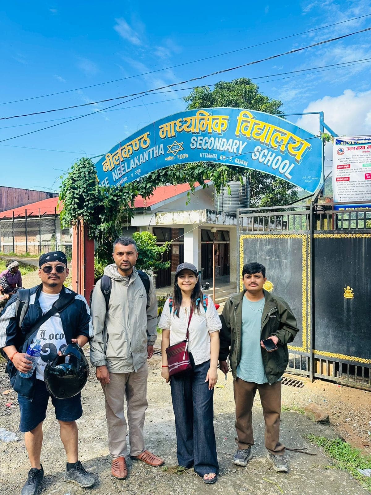 Four members of the team standing under the gate arch of Shree Neelakantha Secondary School, Uttargaya, Rasuwa.