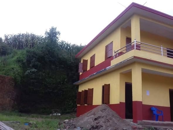 The finished school seen from the side, with a terraced green hillside rising behind it.